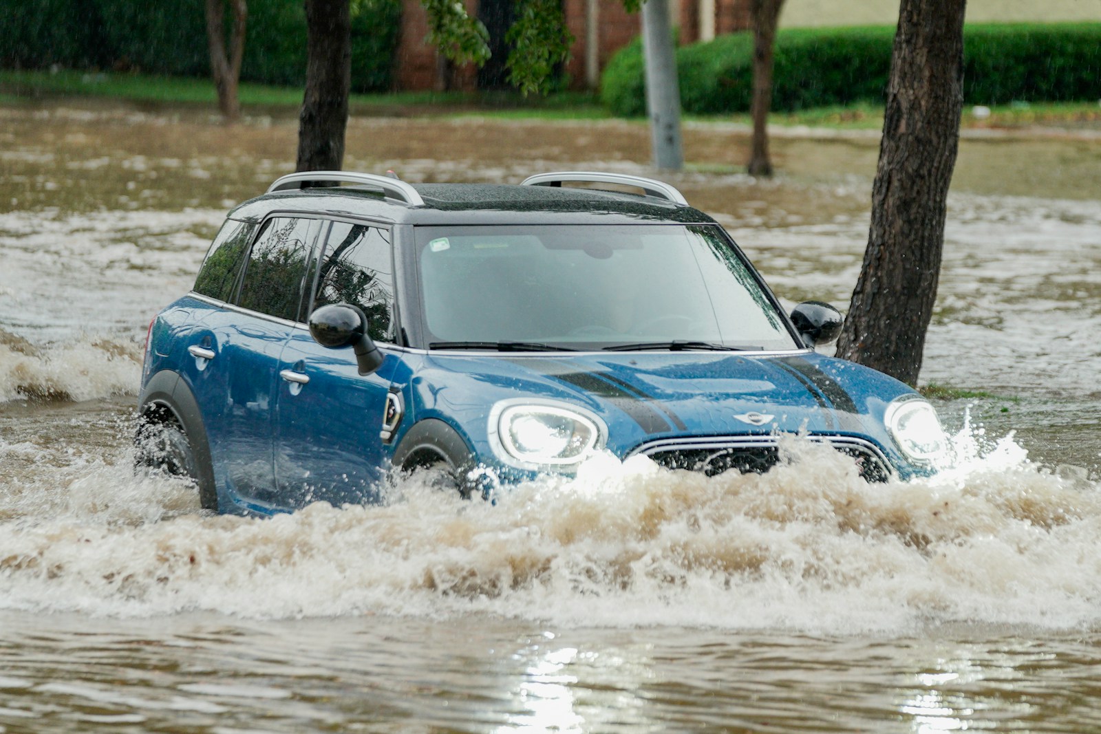 A blue car driving through a flooded street, auto